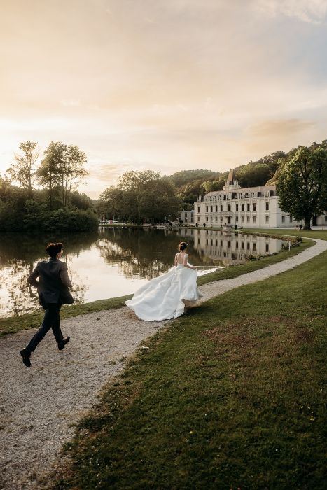 Brautpaar läuft auf das Schloss zu. Im Hintergrund glänzt der See im Sonnenlicht.